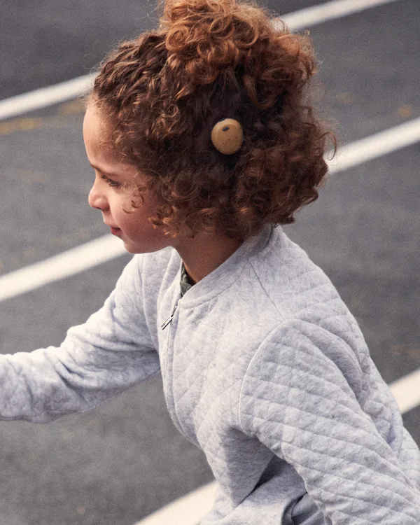 A young girl wearing a bone conduction sound processor, running on a track